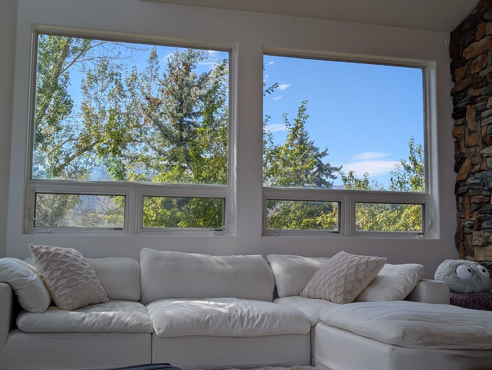 The room at Eden: a white sofa under two wide windows, trees and sky beyond, the stone of the chimney at the edge
